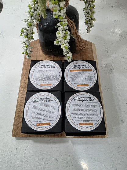 Four black shampoo bars with white labels on a wooden board, surrounded by decorative elements.