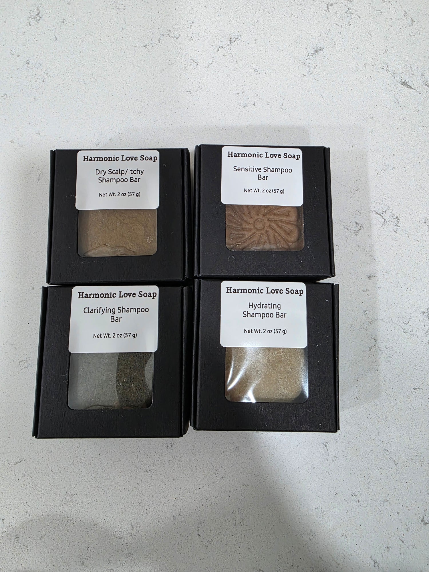 Four black boxes containing soap bars with labels on a light gray surface