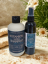Two bottles of Harmonic Love Soap Botanical Loc Shampoo and Scalp Balance Botanical on a textured surface with flowers in the background.
